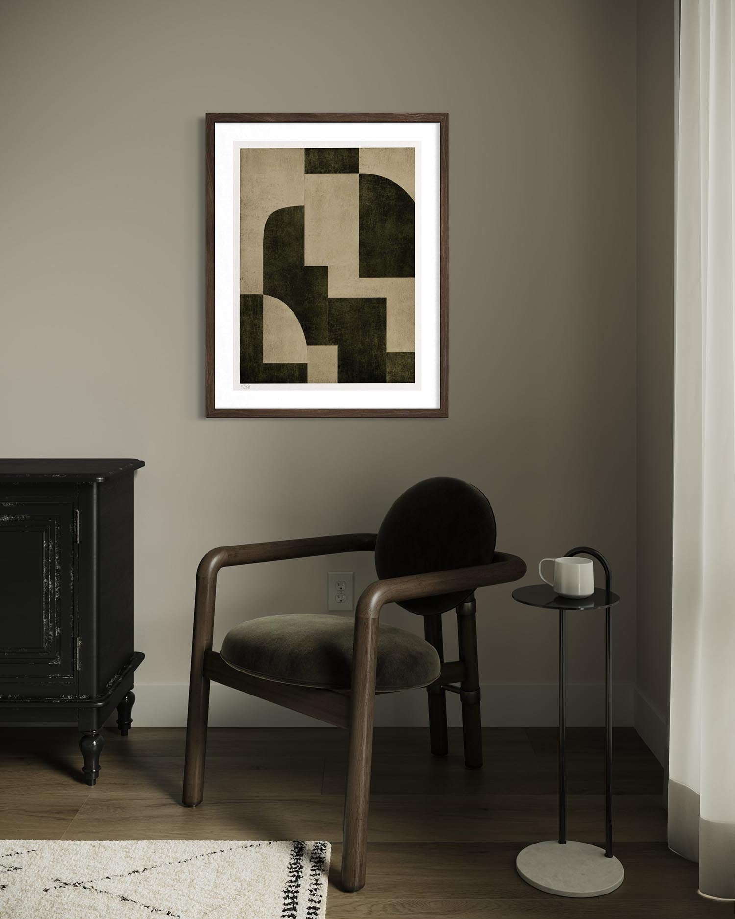 A framed abstract geometric art print hangs on a taupe-gray wall in a styled room setting with a wooden armchair, a black sideboard, and a small side table.