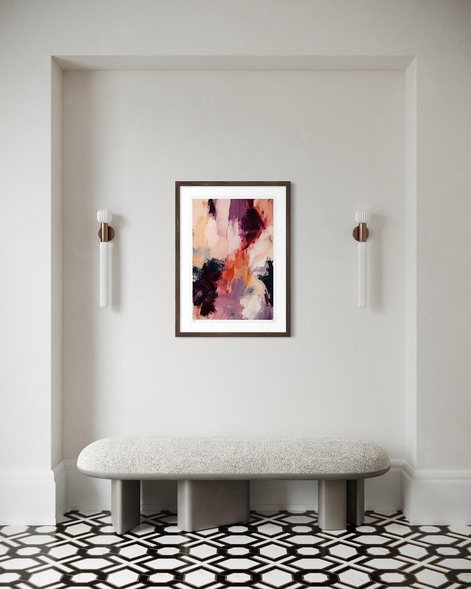 A framed abstract painting with pink, purple, orange, and black brushstrokes hangs on a white wall above a light gray bench in a modern interior setting with black and white geometric tile flooring.
