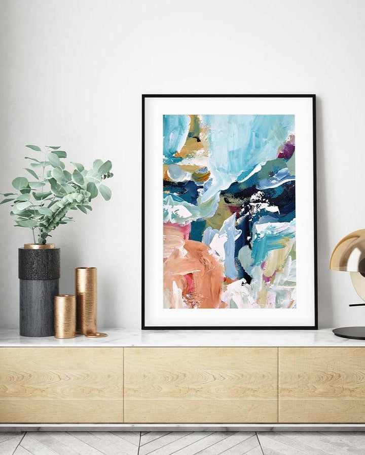 Framed abstract art print on a wall above a wooden cabinet with decorative items.
