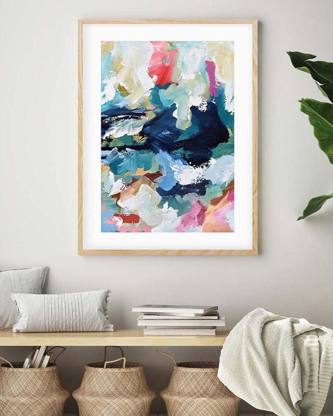 Colorful abstract painting in a wooden frame on a wall above a wooden bench with decorative items.