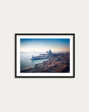Framed photograph of a cityscape with a large building and water body on a white wall.