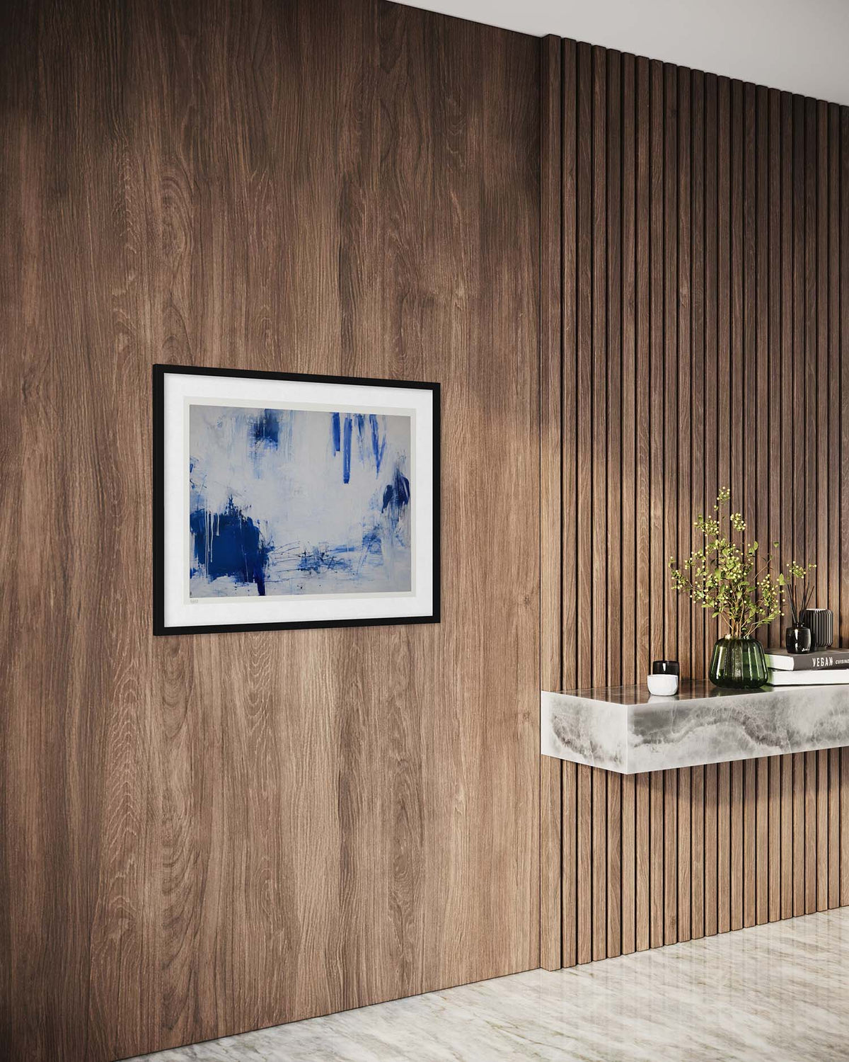 A framed abstract art print with blue and white brushstrokes hangs on a dark wood-paneled wall in a modern interior setting with a floating shelf and marble accents.