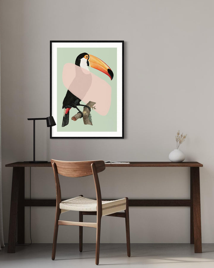 Framed artwork of a toucan on a wall above a desk with a chair.