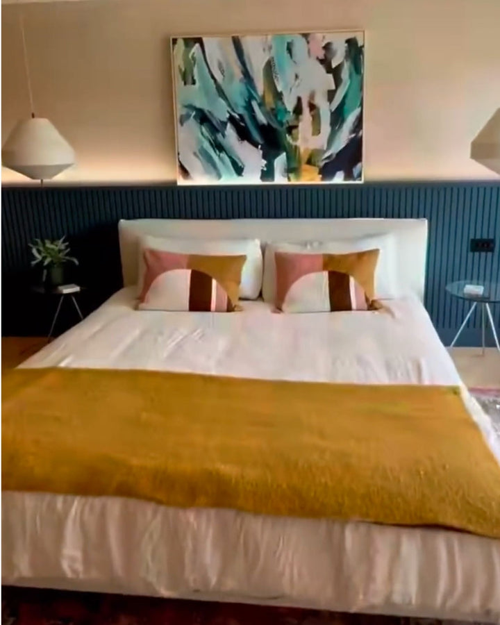 Bedroom with a bed featuring yellow blanket and colorful pillows, abstract painting on the wall.