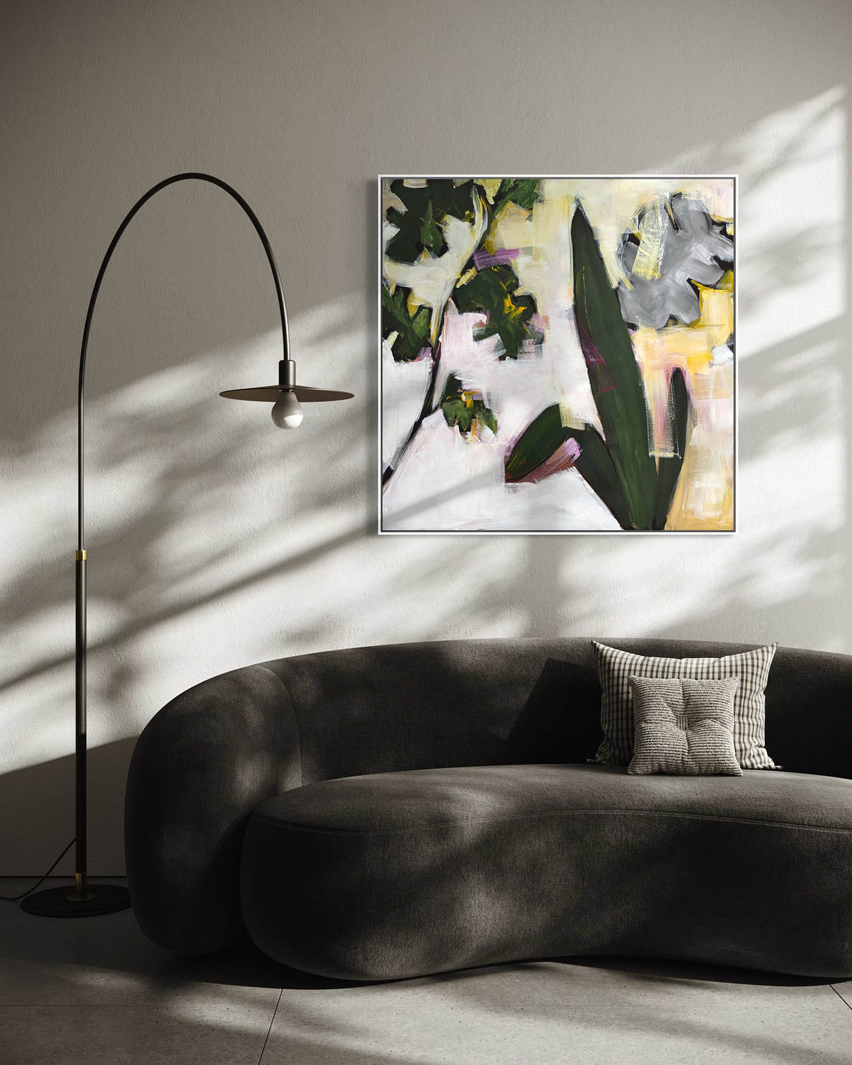 An abstract floral canvas print with green leaves, gray flowers, and yellow accents, displayed on a light gray wall above a dark gray curved sofa in a modern living room setting with a black floor lamp.