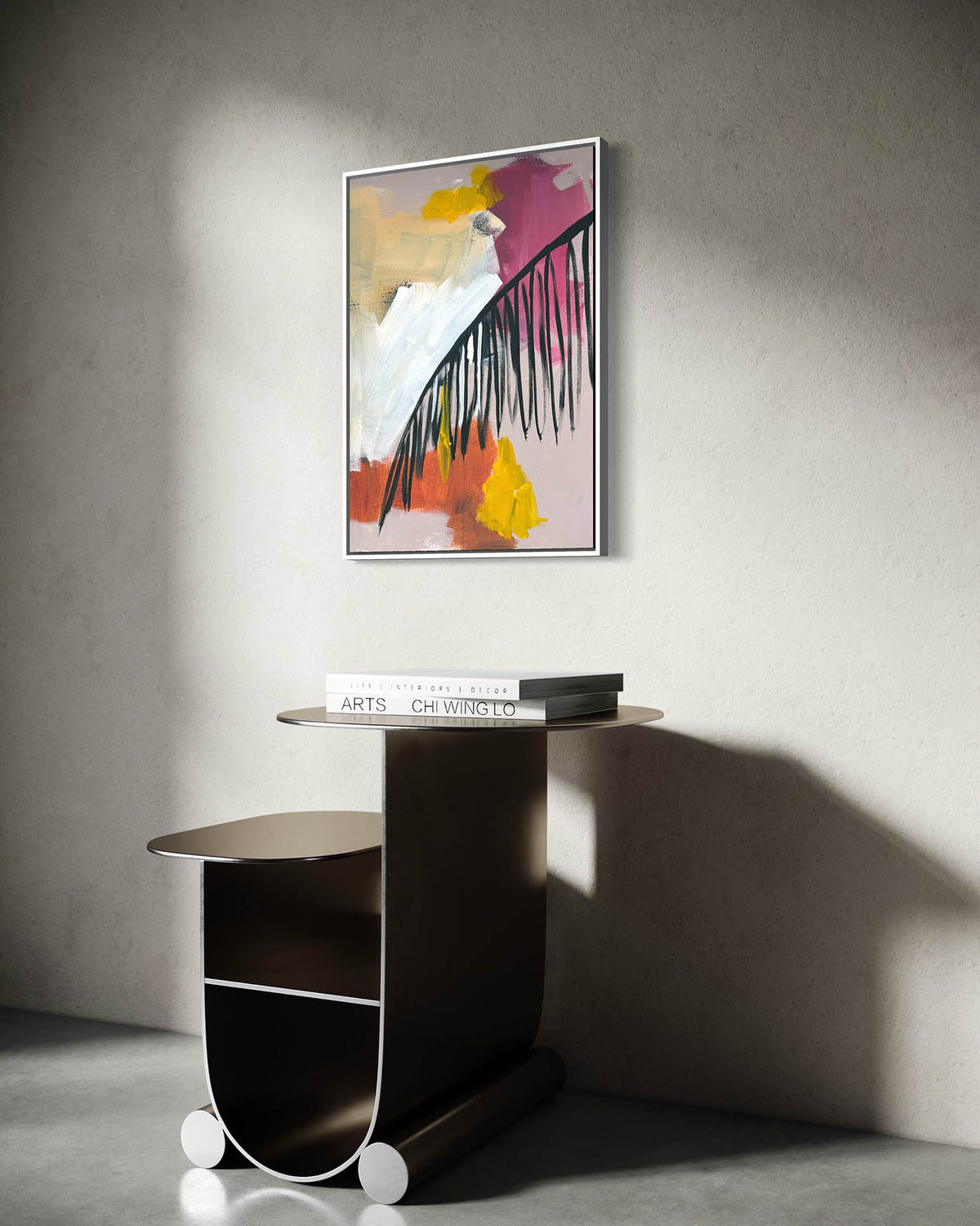 A framed abstract art print with pink, yellow, white, and black brushstrokes hangs on a textured gray wall above a dark modern side table with books.