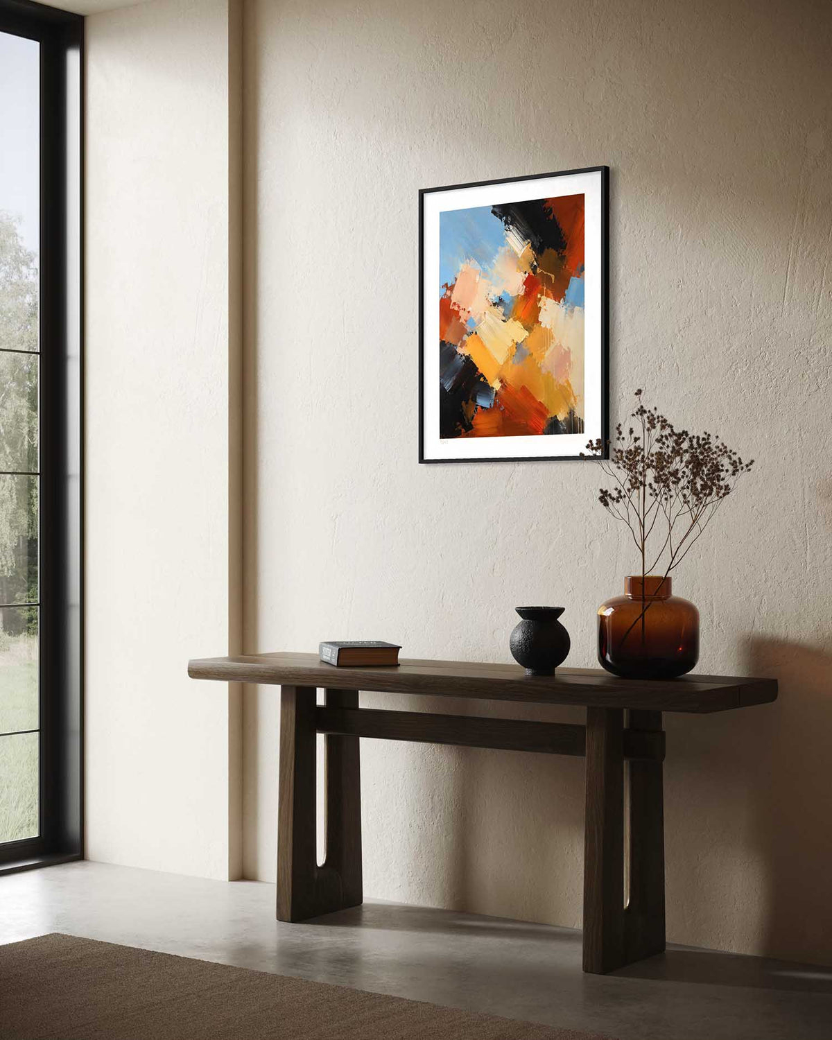 A framed abstract art print with orange, blue, black, and white brushstrokes hangs on a beige wall above a dark wood console table with decorative vases and a small book.