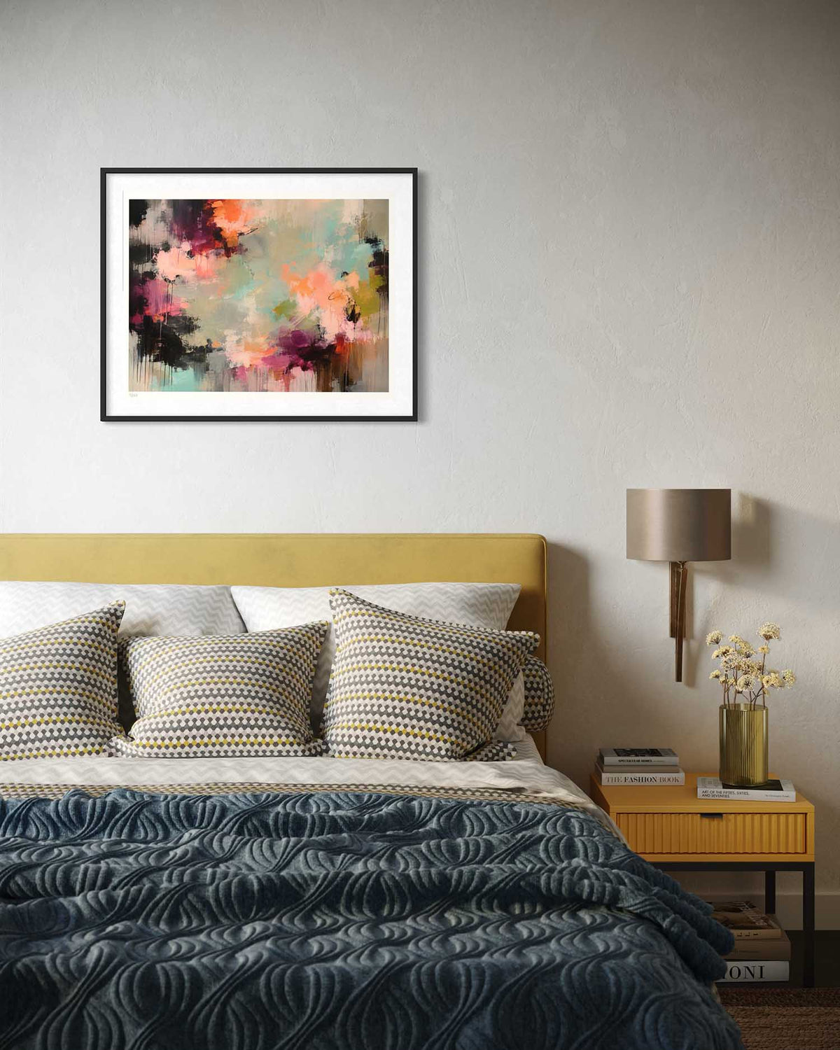 A framed abstract wall art print hangs above a bed in a styled bedroom. The artwork features a multicolor abstract design with pink, orange, purple, black, and teal tones.