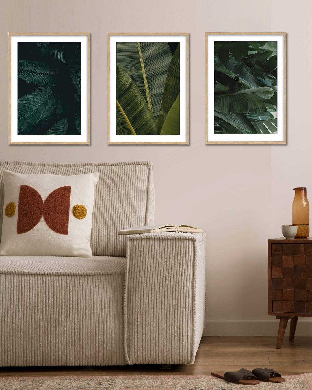 Three framed leaf prints on a wall above a sofa with decorative pillows.