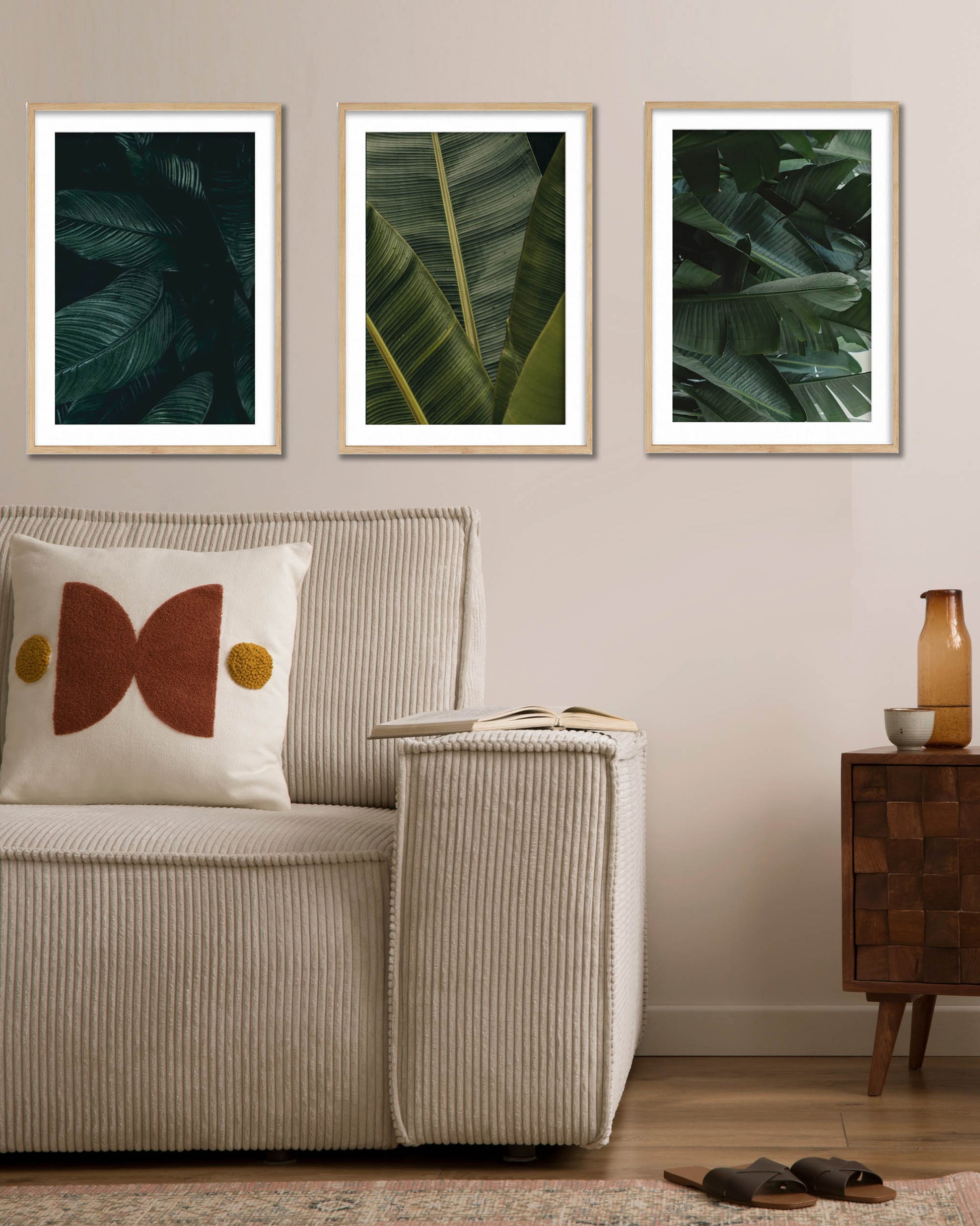 Three framed leaf prints on a wall above a sofa with decorative pillows.