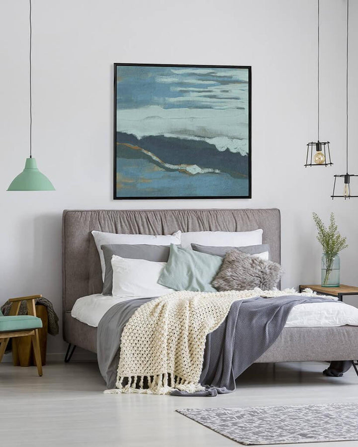 Modern bedroom with gray upholstered bed, colorful bedding, and abstract art on the wall.