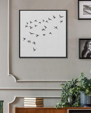 Framed artwork of birds on a white background in a room with decor elements.