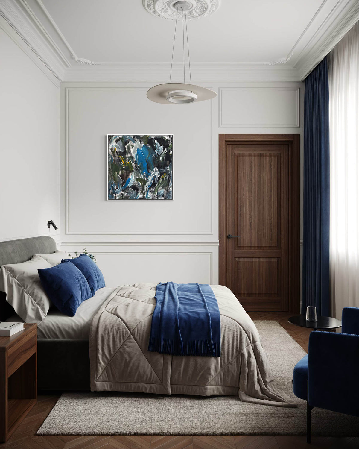 A styled bedroom interior featuring a bed dressed in beige bedding with a blue throw and blue pillows, set against white paneled walls. A blue abstract painting hangs above the bed, next to a dark wood door and a dark blue curtain.