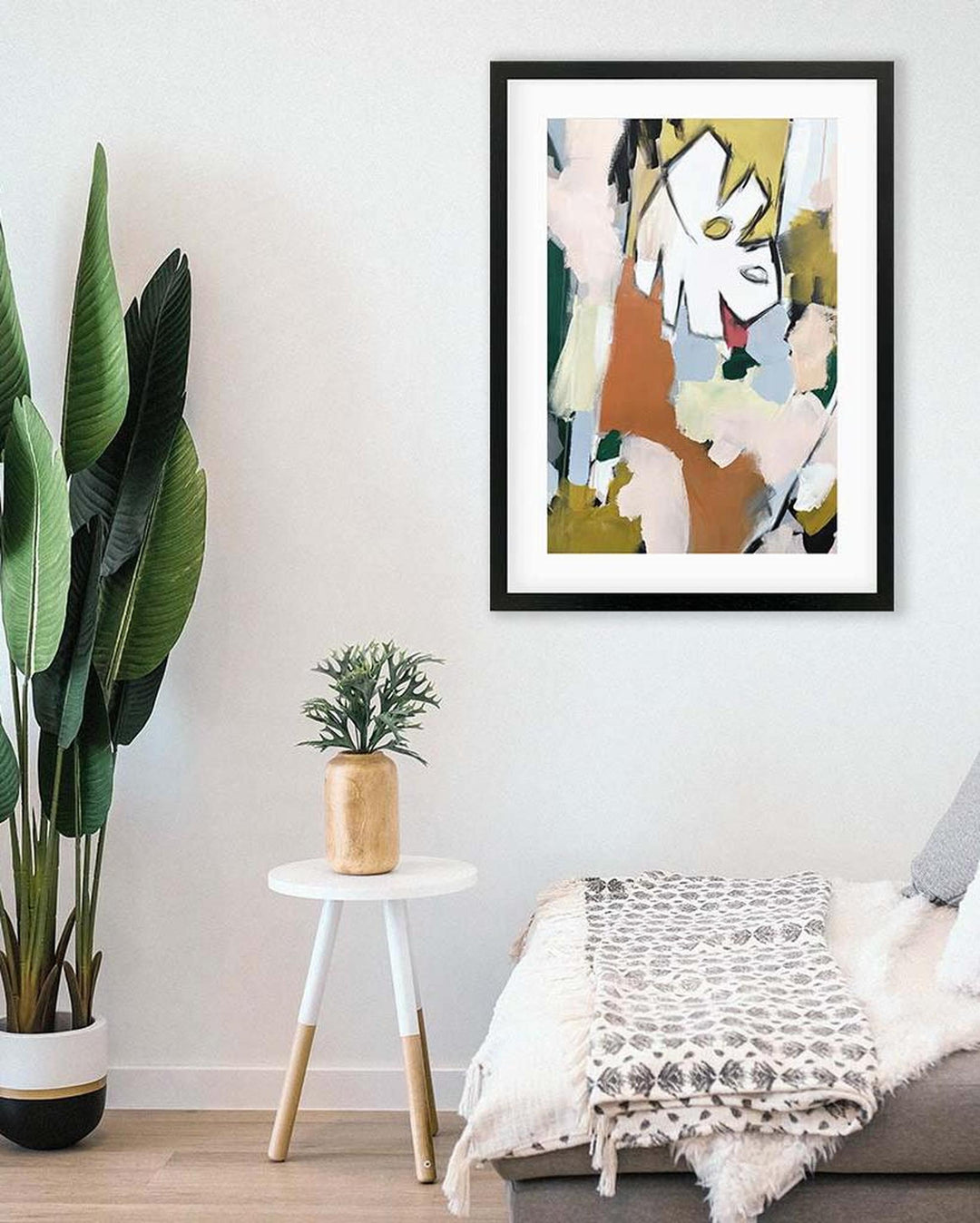 Framed abstract art print on a wall above a sofa with decorative plants.
