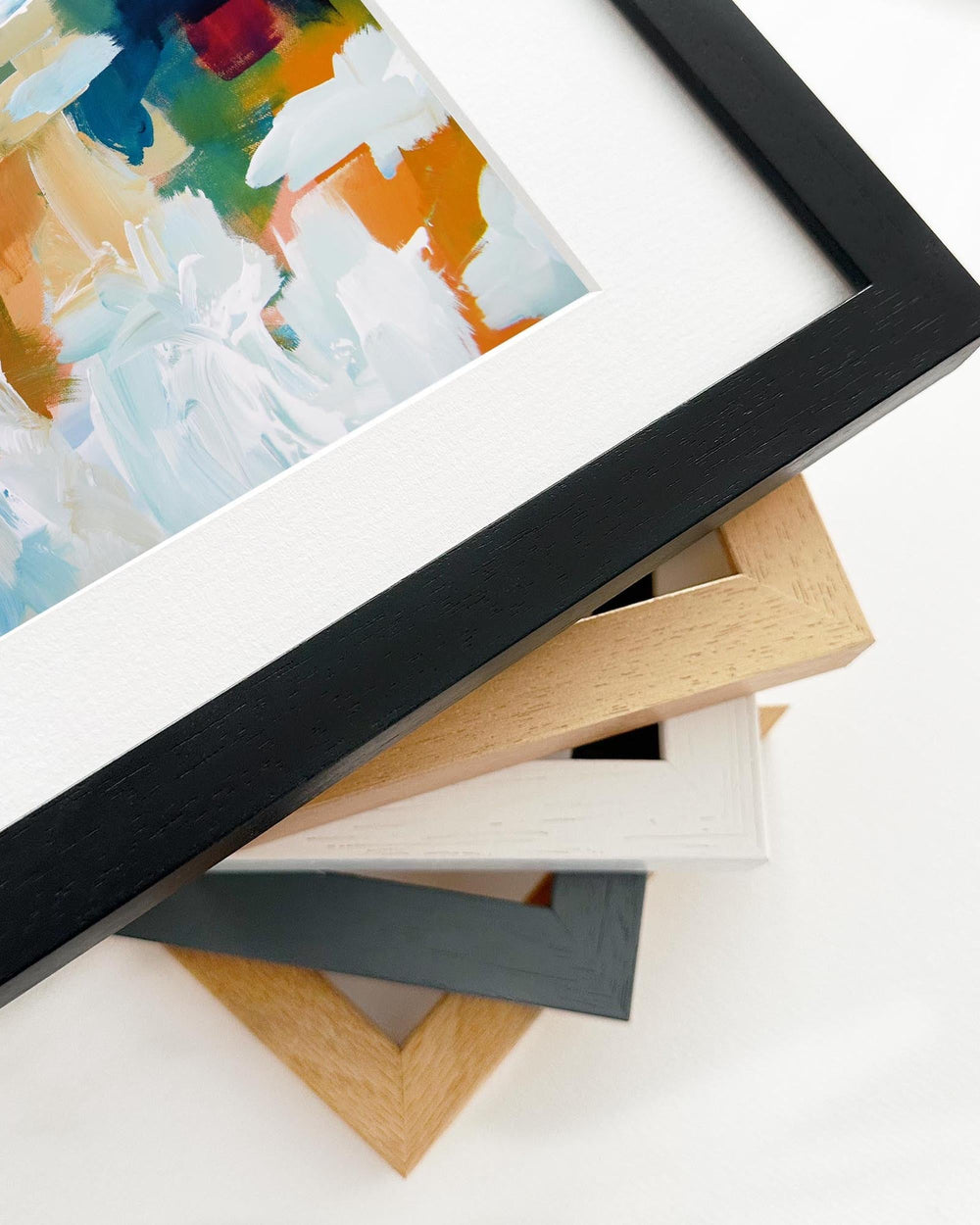 Close-up of a framed painting with various picture frames on a white surface