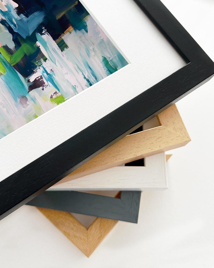 Close-up of a black picture frame with a painting inside, surrounded by other frames on a white surface.