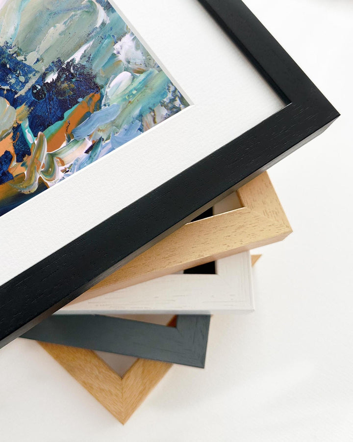 Stack of variously framed artworks on a white surface