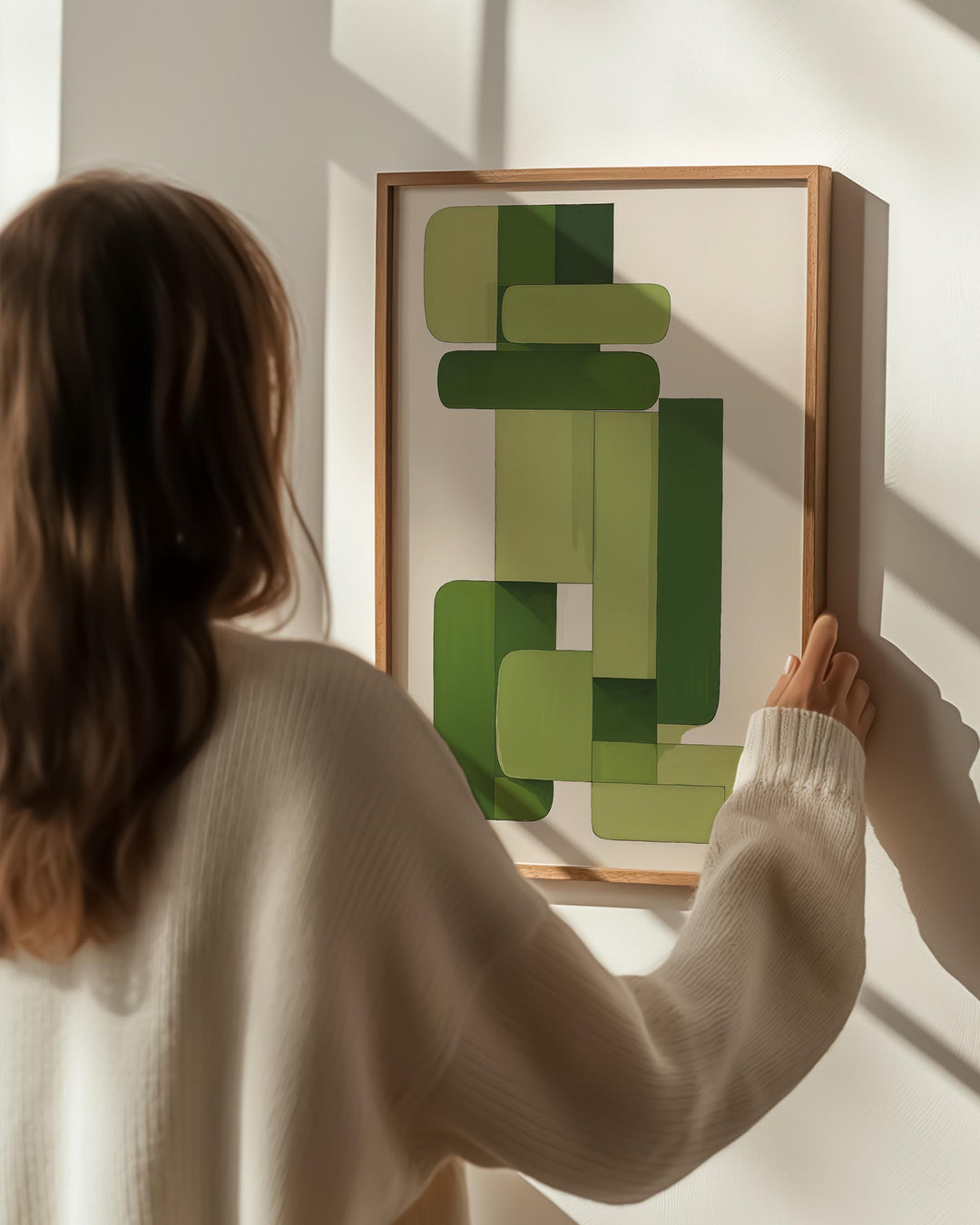 woman holding and hanging green abstract framed poster on wall 