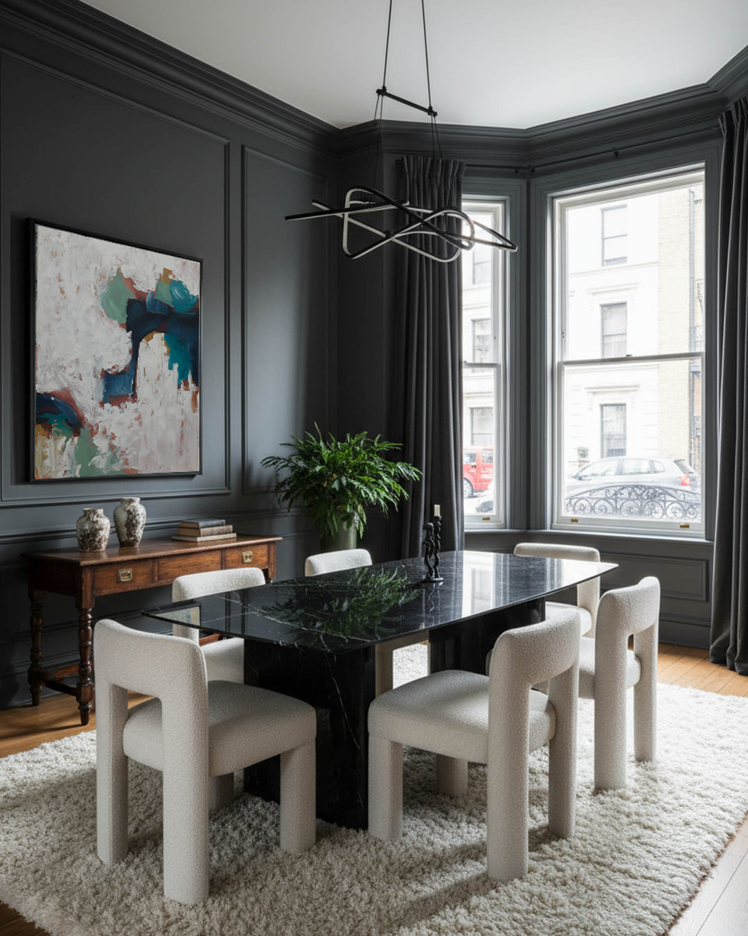 Modern dining room with dark marble table and white chairs, large windows, and abstract art on the wall.