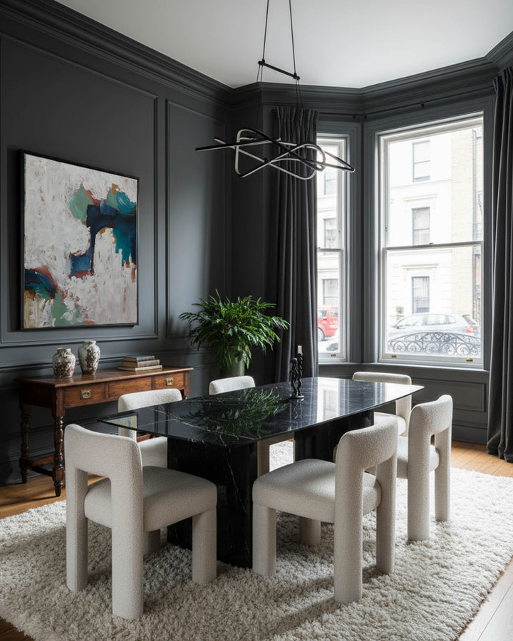 Modern dining room with dark marble table and white chairs, large windows, and abstract art on the wall.