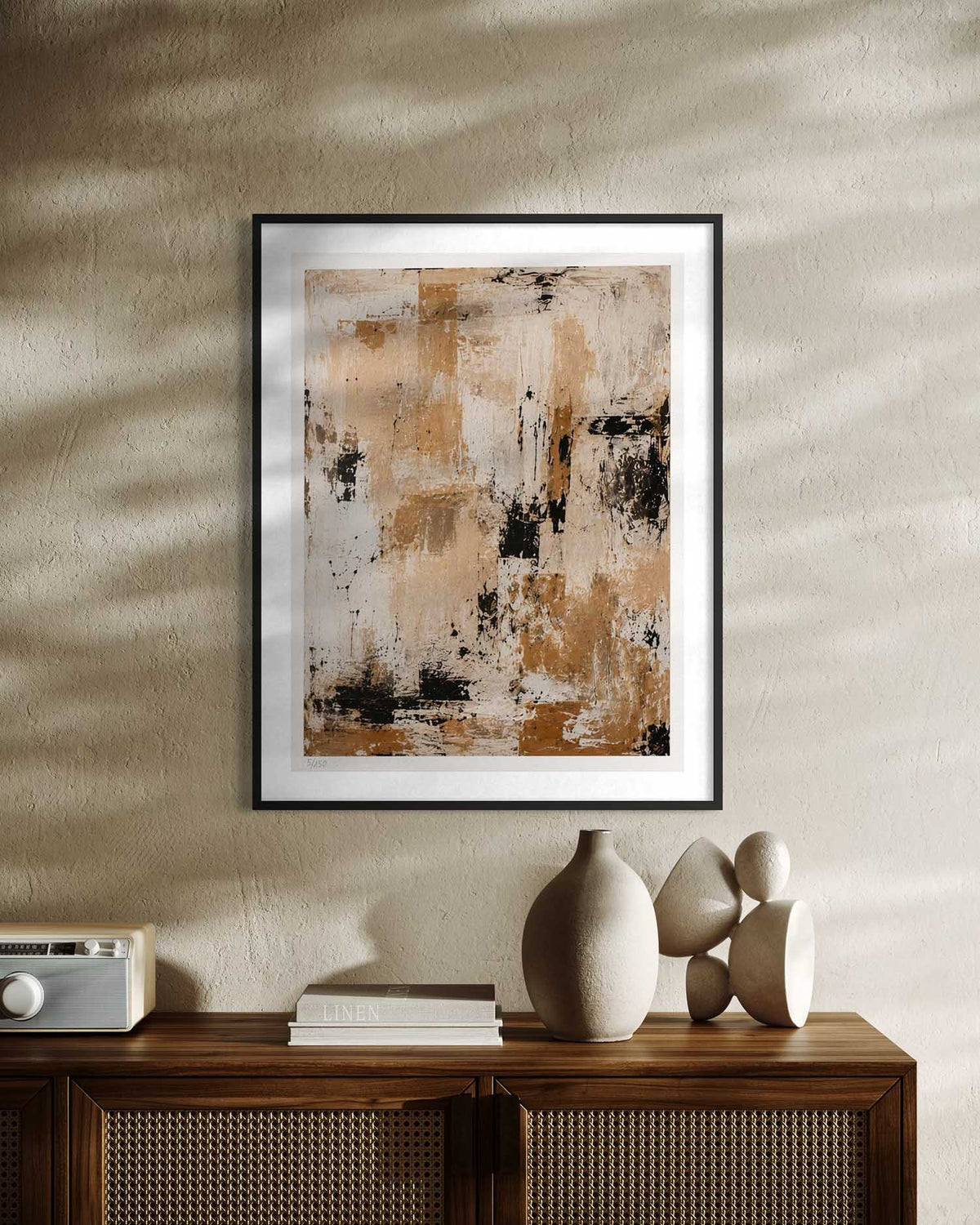 A framed abstract art print with a black frame and white mat, hanging on a textured beige wall above a wooden console table with decorative ceramic vases and books.