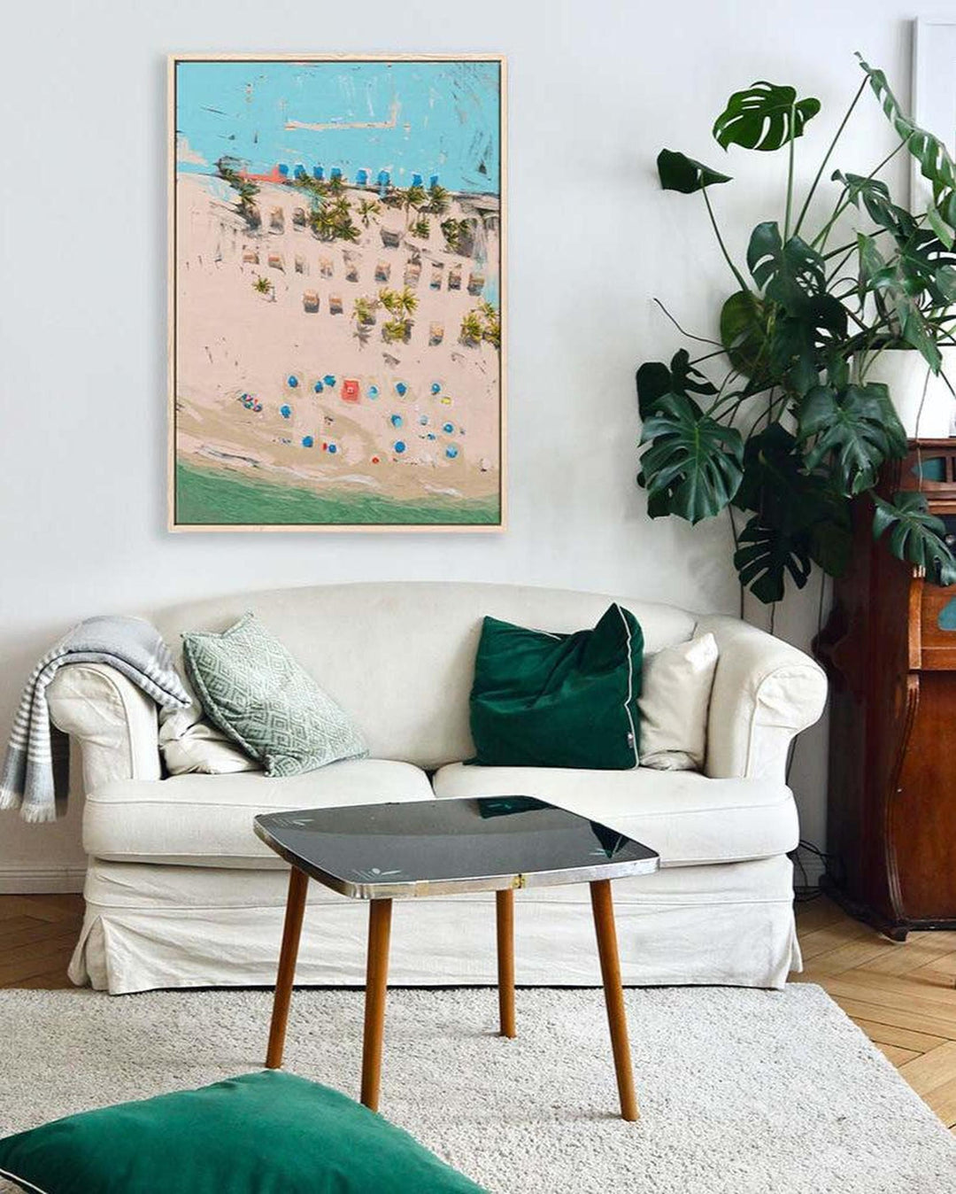 Living room with a white sofa, green cushions, and a framed artwork on the wall.