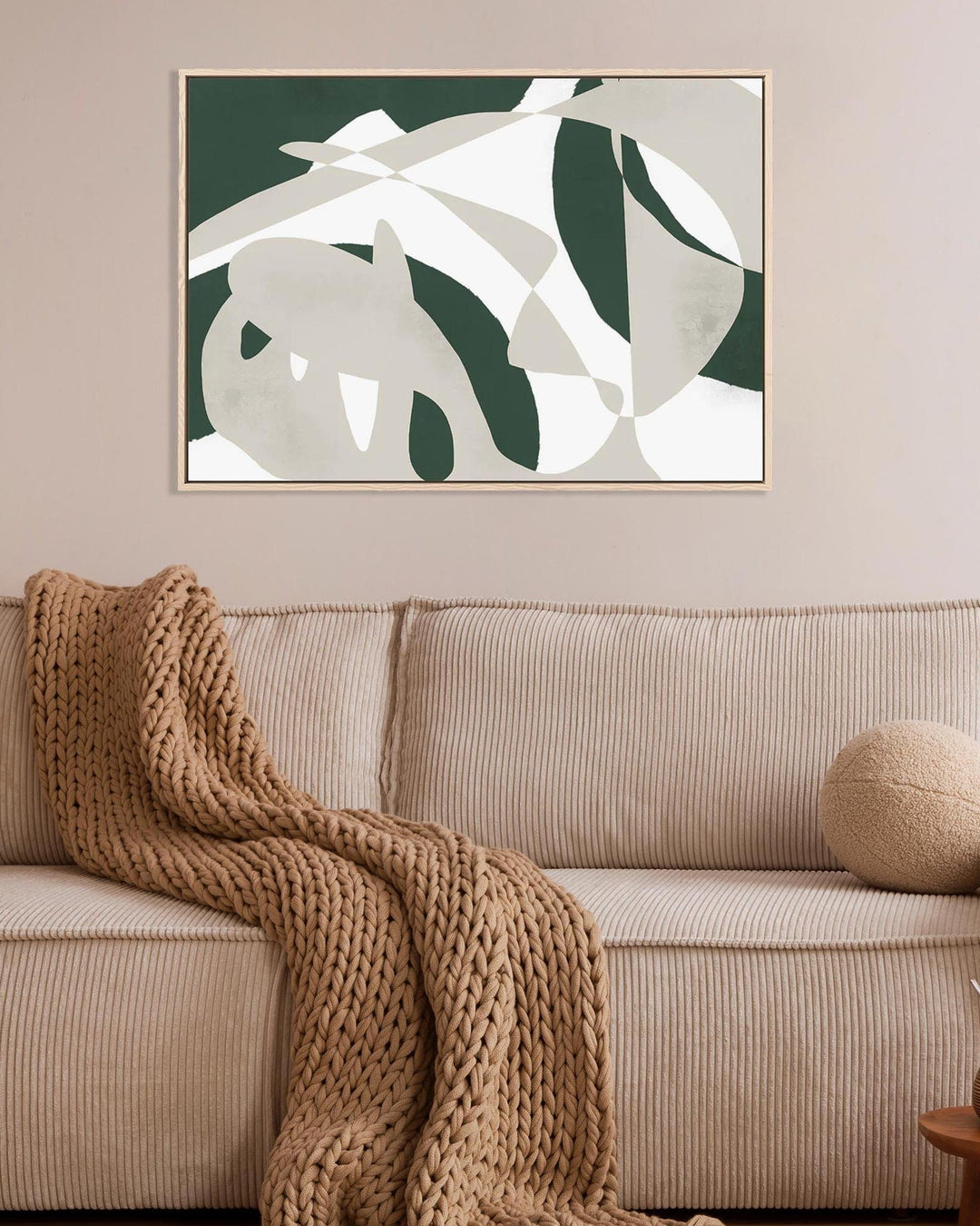 Beige sofa with a knitted blanket and decorative items, featuring a abstract leaf-patterned artwork on the wall.