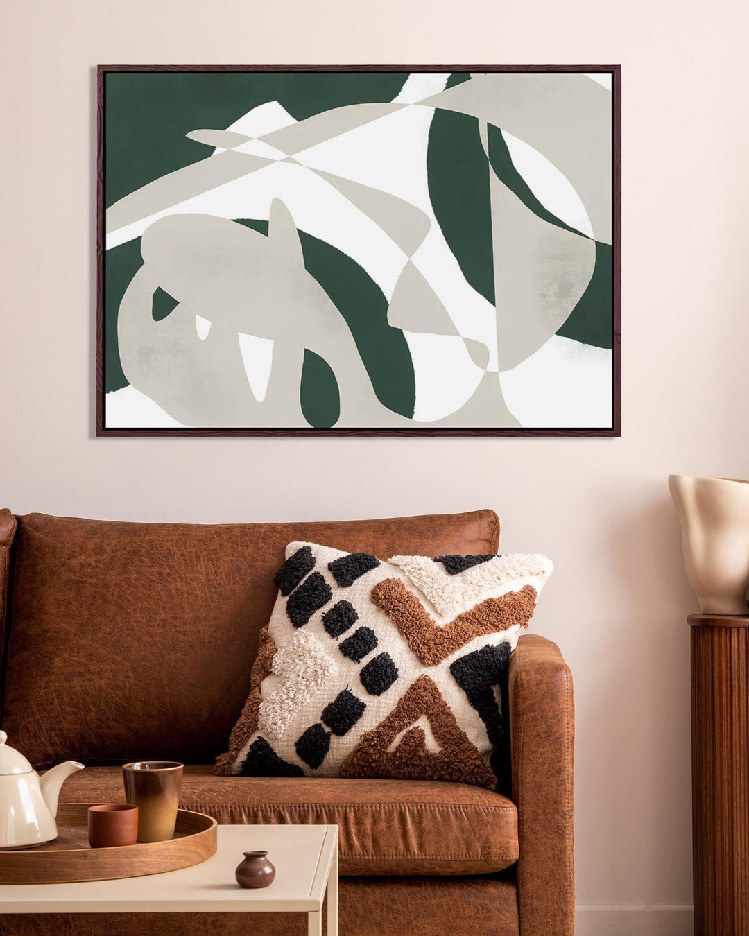 Living room with a brown sofa, decorative pillow, and abstract leaf art on the wall.