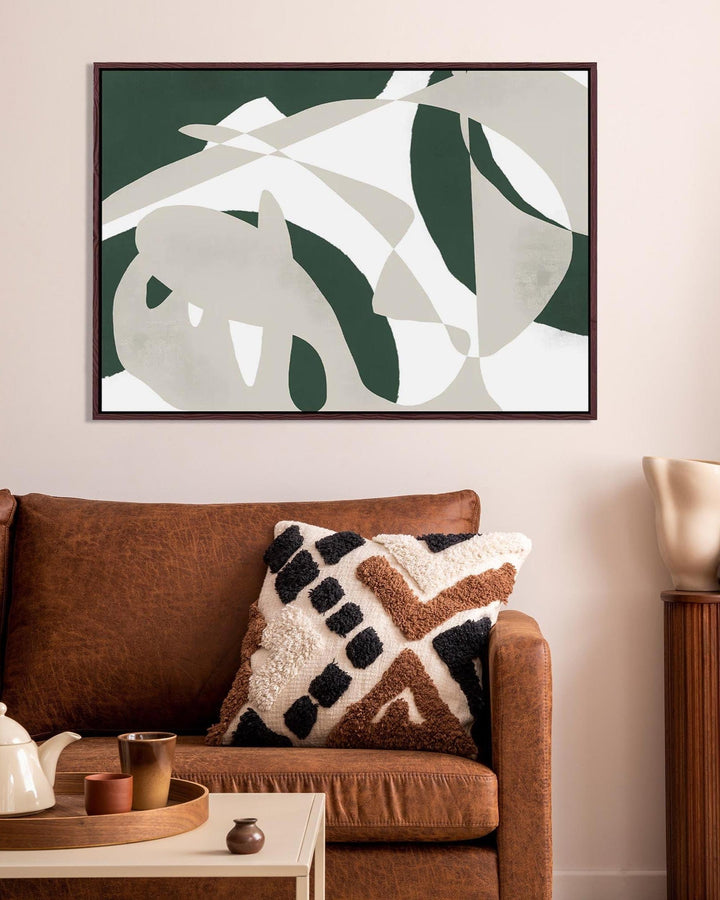 Living room with a brown sofa, decorative pillow, and abstract leaf art on the wall.