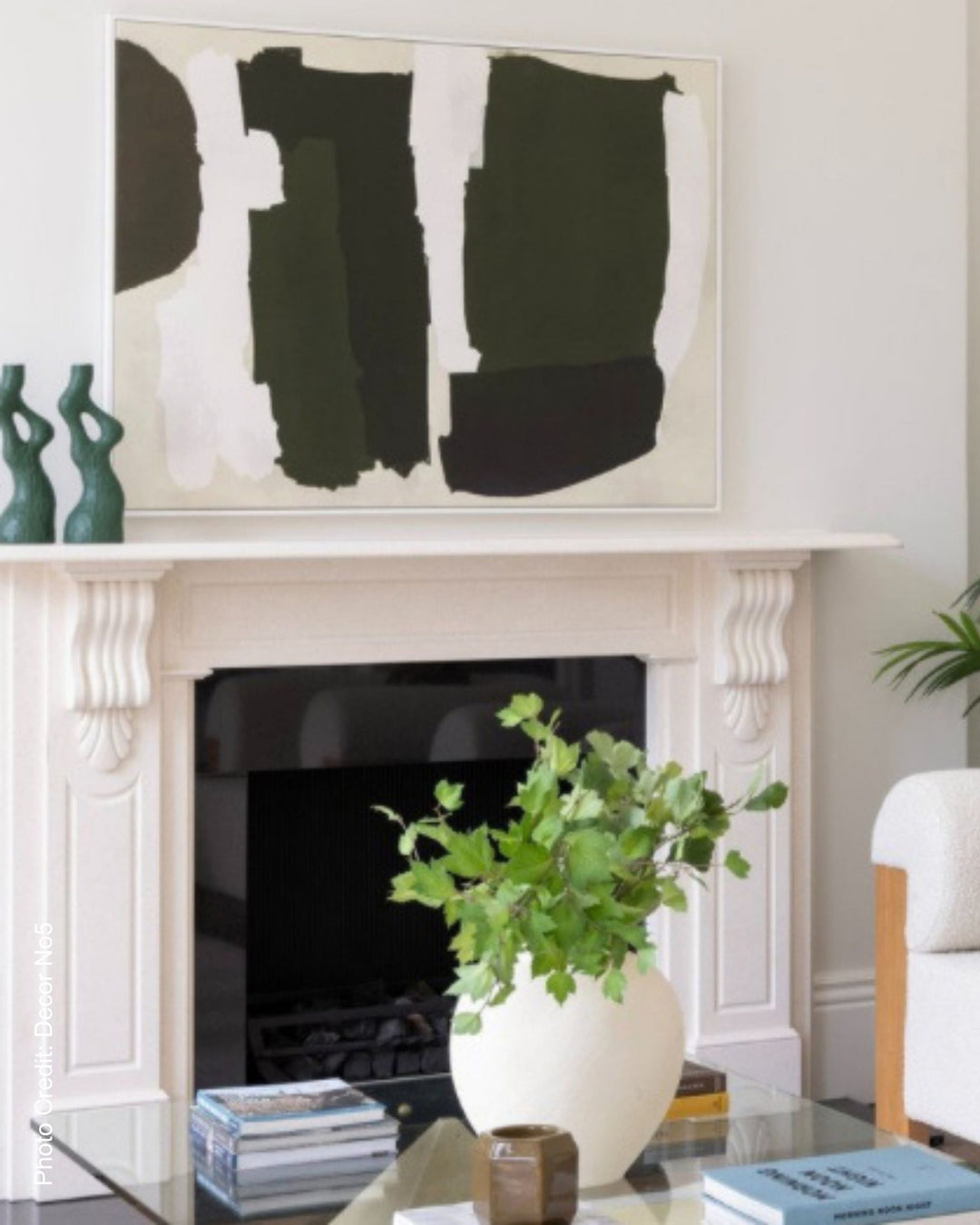 Modern luxury living room with abstract art above a fireplace, plant on a table, and books.