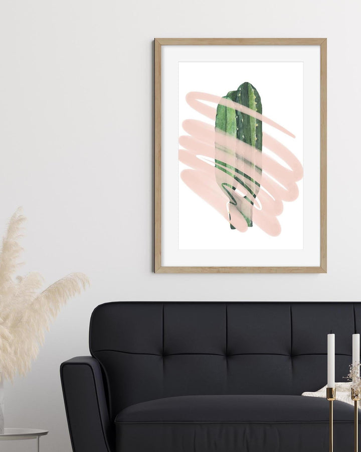 Framed abstract art print with green and pink brushstrokes above a black sofa.