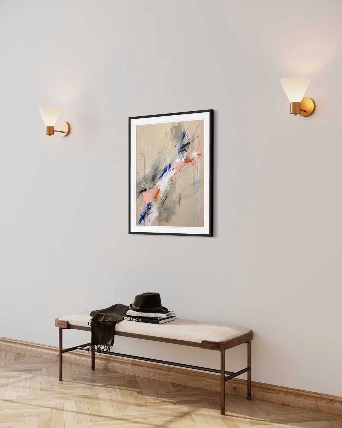 A framed abstract art print hangs on a light gray wall in a modern entryway setting, with a bench below and two wall sconces on either side. The artwork features a beige background with sweeping brushstrokes in blue, pink, gray, and white.