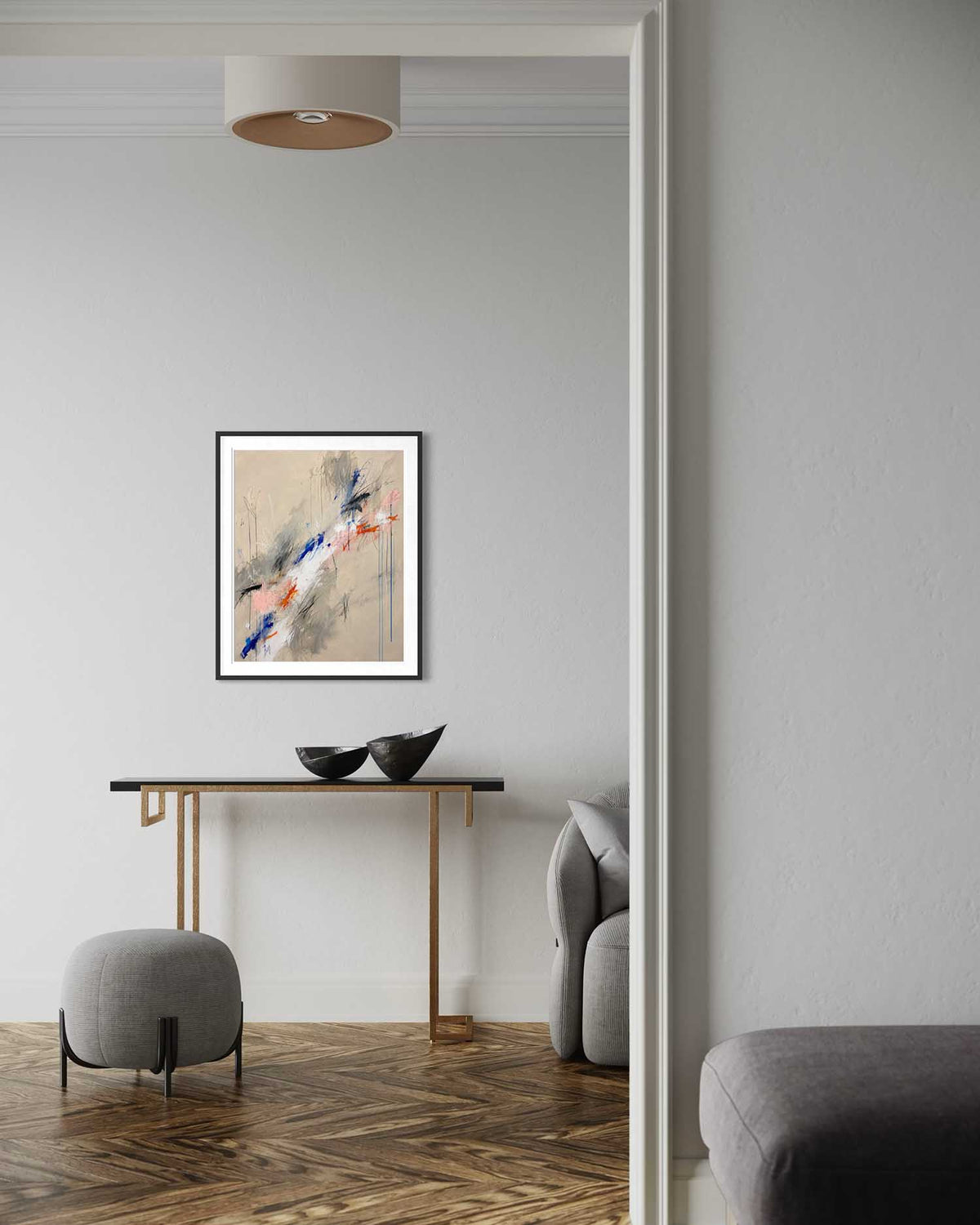A framed abstract art print with blue, red, and gray brushstrokes on a beige background, displayed on a light gray wall in a modern living room setting above a console table.