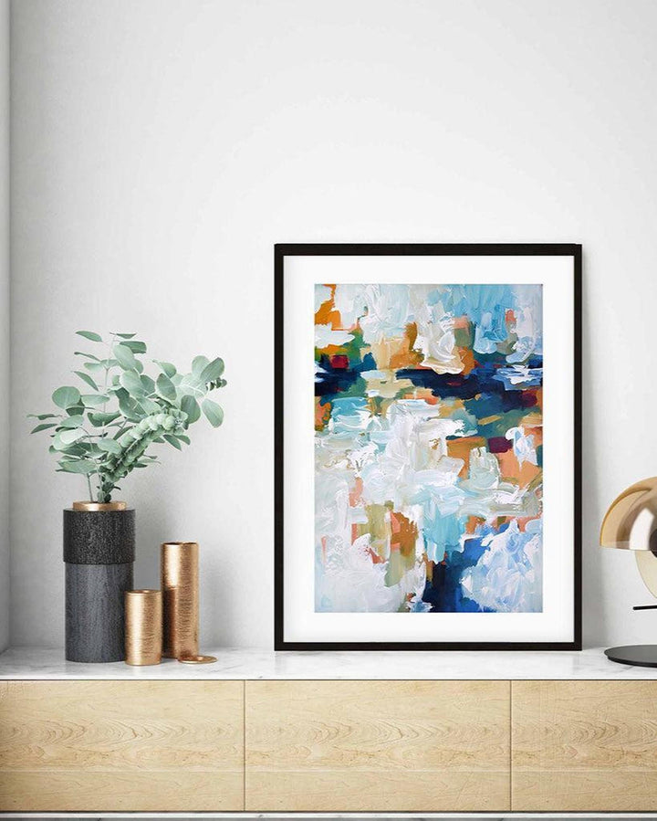 Framed abstract art piece on a wall with decorative vases and a plant below.