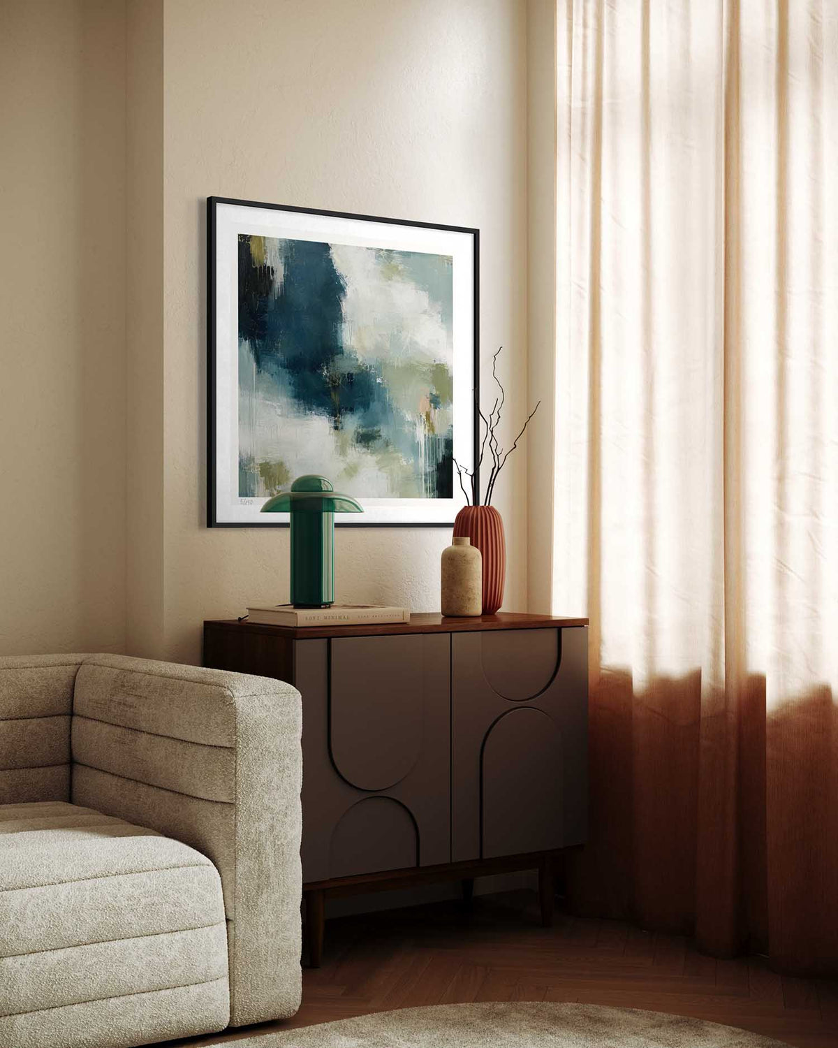 A framed abstract art print with blue, green, and white tones hangs on a beige wall above a dark wood sideboard in a styled living room setting.