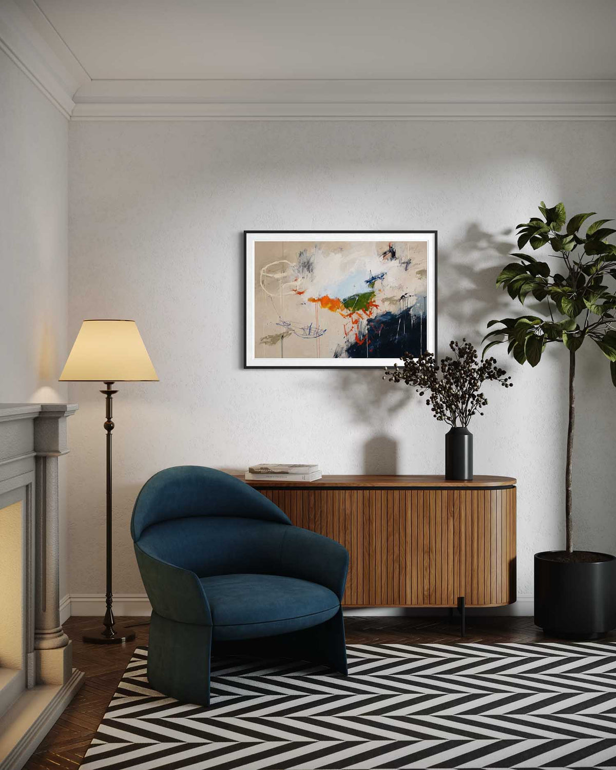 A framed abstract art print hangs on a light gray wall above a wooden console table in a styled living room. The room includes a blue velvet armchair, a floor lamp, a potted plant, and a black-and-white patterned rug.