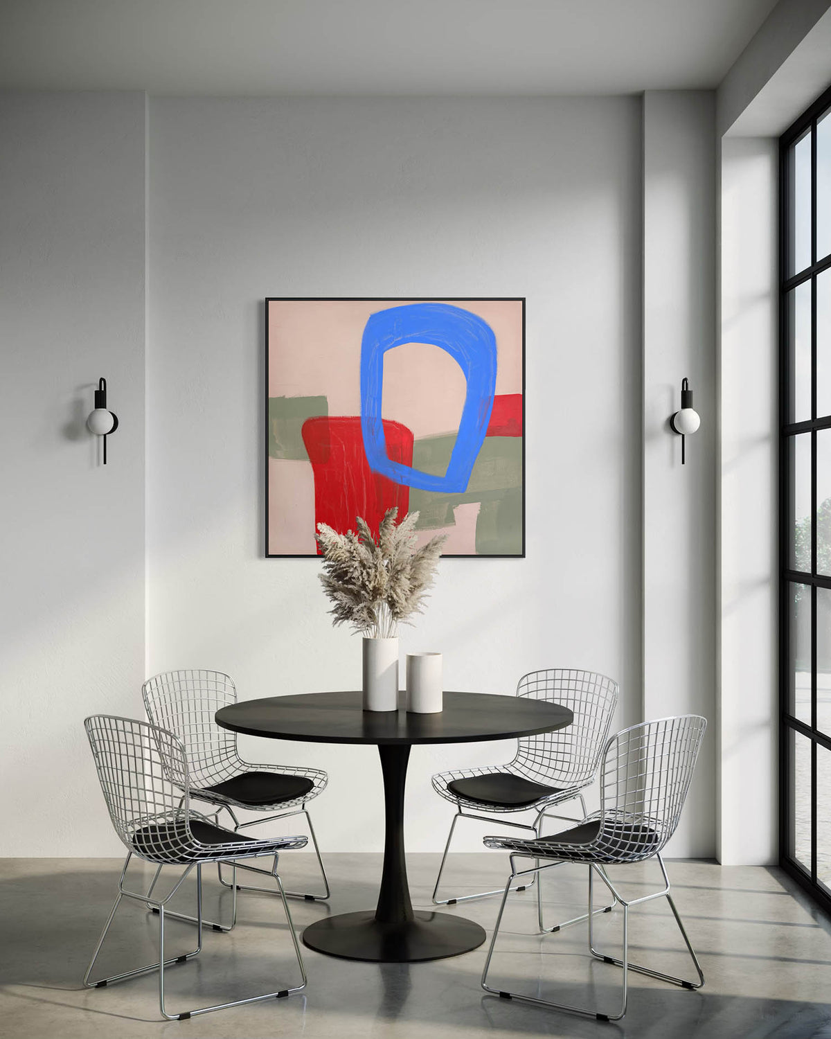 A modern dining room setup featuring a black round pedestal table surrounded by four wire mesh chairs with black seat cushions. Above the table hangs a framed abstract painting with bold blue, red, green, and beige shapes.