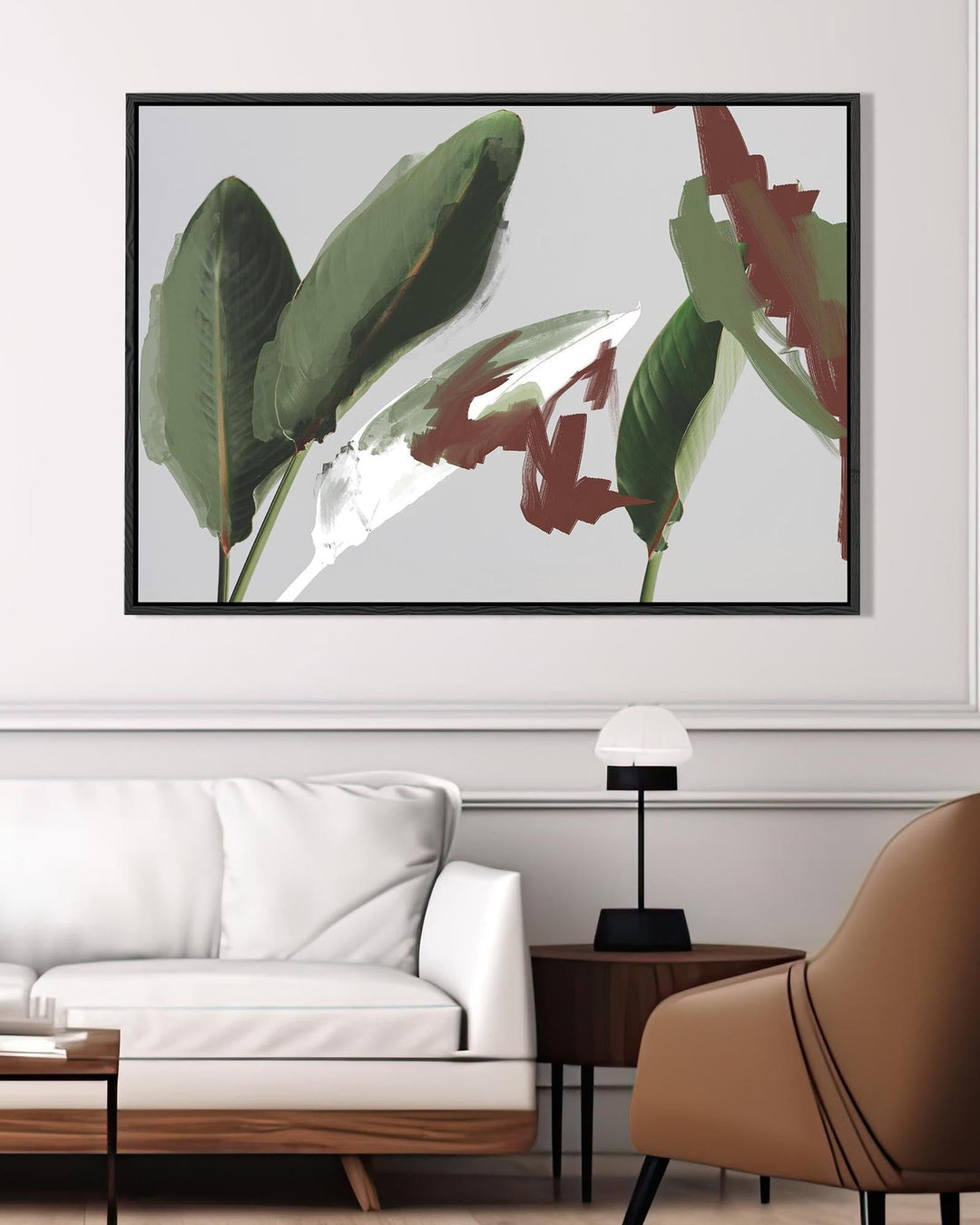 Framed artwork of leaves above a modern living room with a white sofa and brown chair.