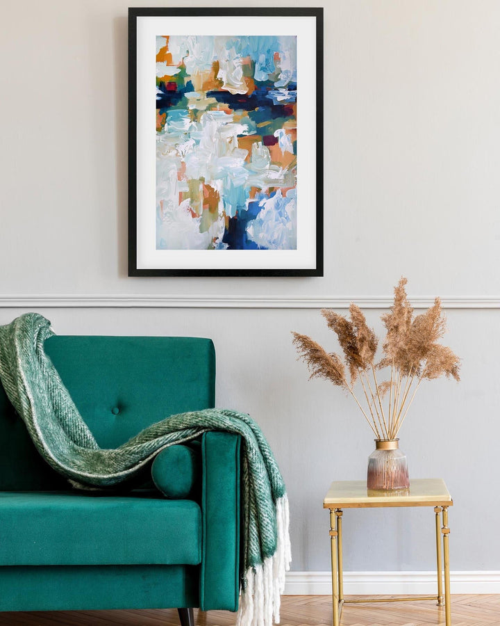 Teal armchair with a green blanket, gold side table with dried plants, and abstract art on the wall.
