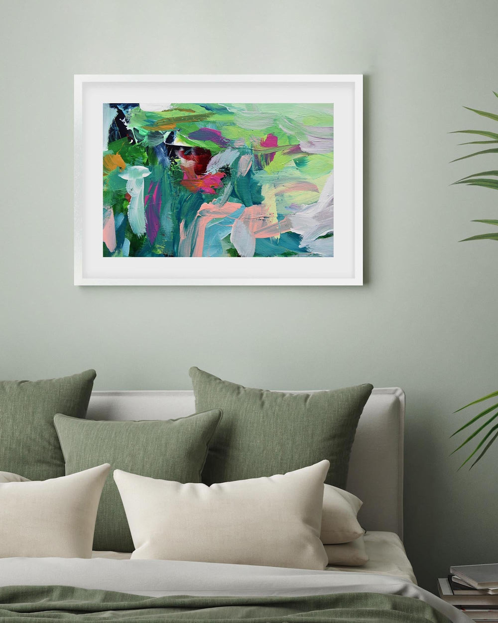 Framed abstract painting on a wall above a bed with green and white pillows.