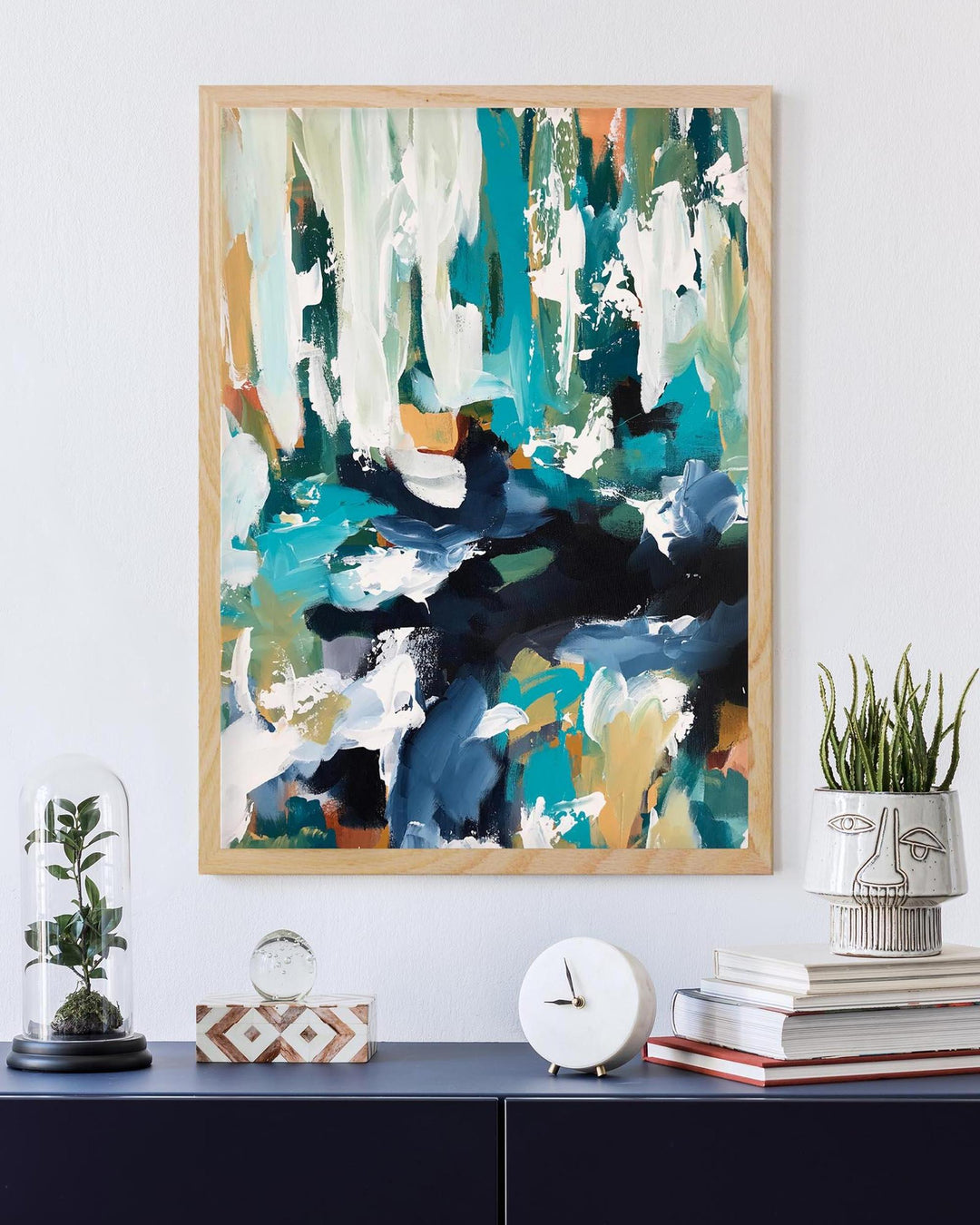 Abstract painting in a wooden frame on a wall with decorative items below.