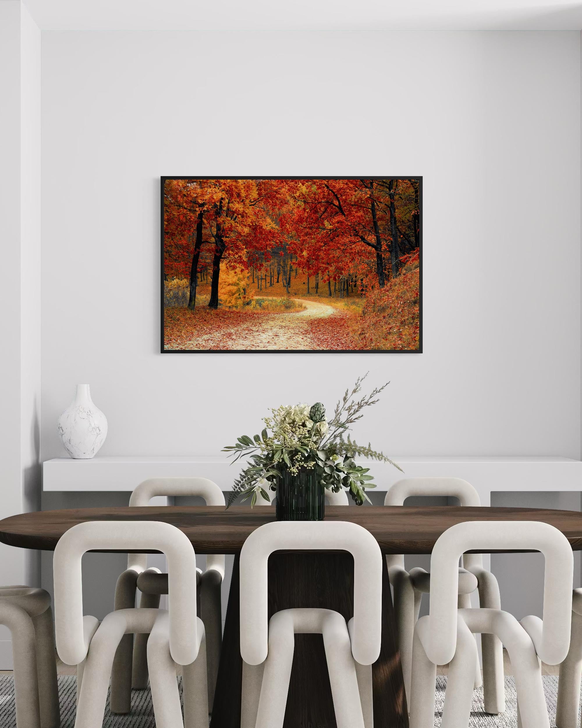 Framed artwork of a forest scene with autumn leaves above a dining table with chairs.