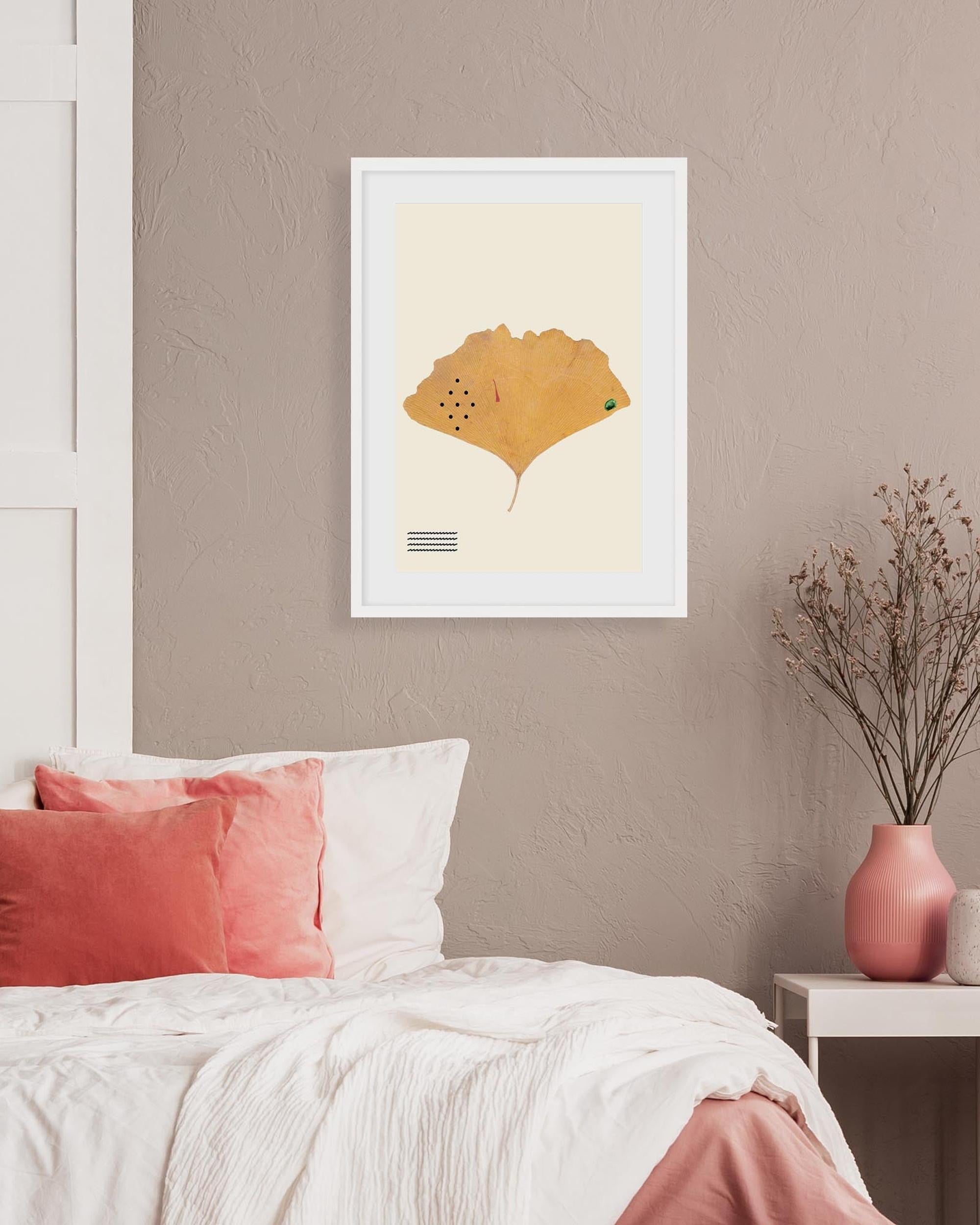 Framed artwork of a yellow leaf on a beige wall above a bed with pink and white pillows.