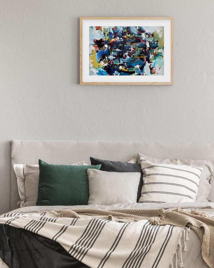 Framed abstract painting above a bed with pillows and a blanket.