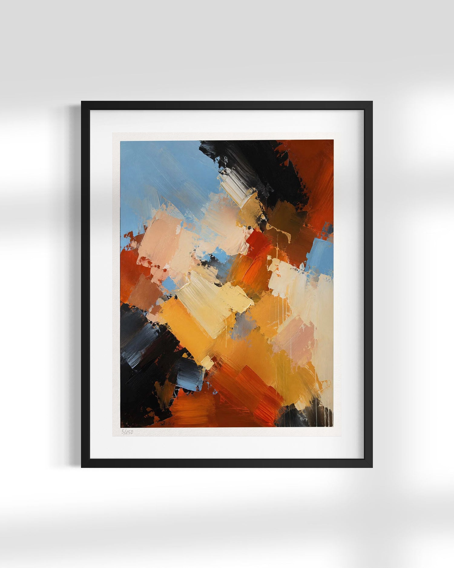 A framed abstract art print featuring expressive brushstrokes in orange, yellow, blue, black, and cream, presented in a black frame with a white mat against a light gray wall.