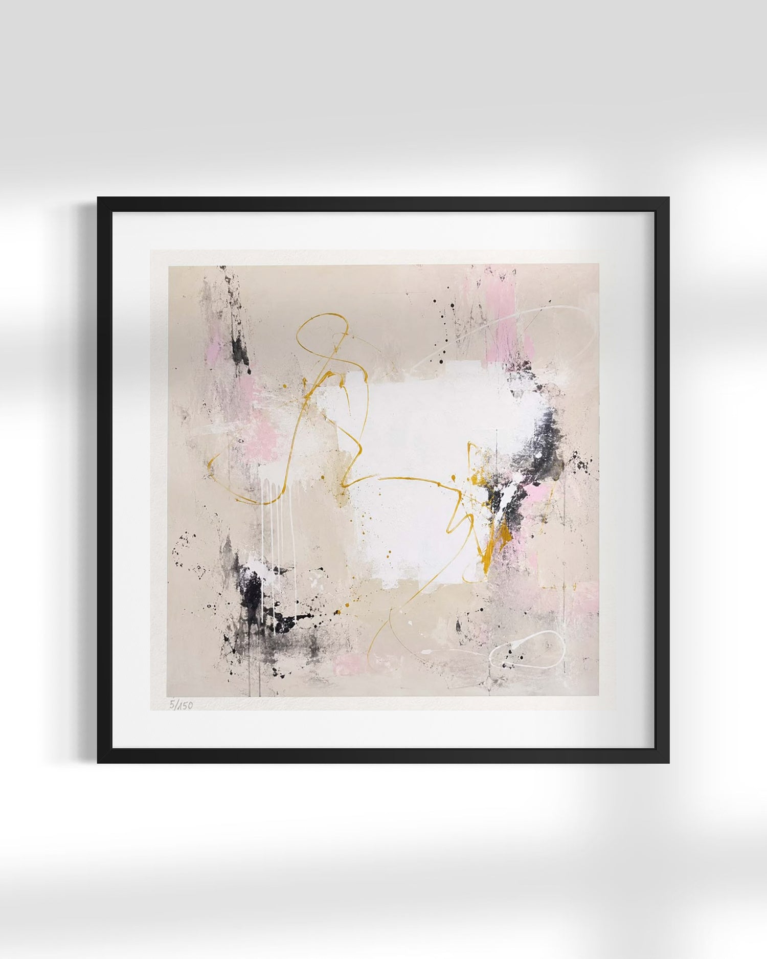Framed abstract wall art featuring a minimalist composition with a white center, soft pink and beige brushstrokes, black paint splatters, and gold line details, presented in a black frame against a light gray wall.