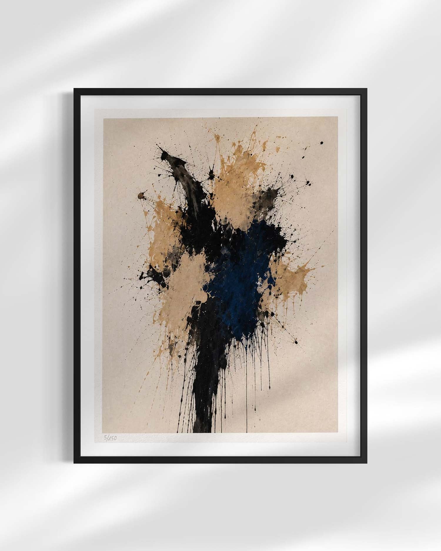 Framed abstract art print featuring a black and navy blue paint splatter design on a beige background, displayed in a black frame with a white mat against a light gray wall with soft leaf shadows.