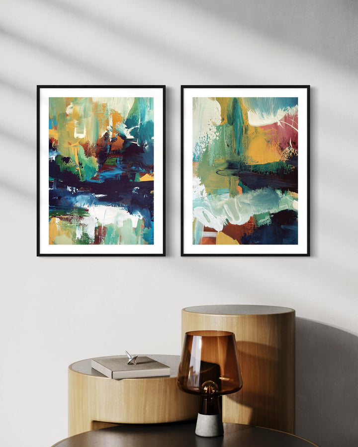 Two abstract art prints on a wall above a wooden side table with a lamp.