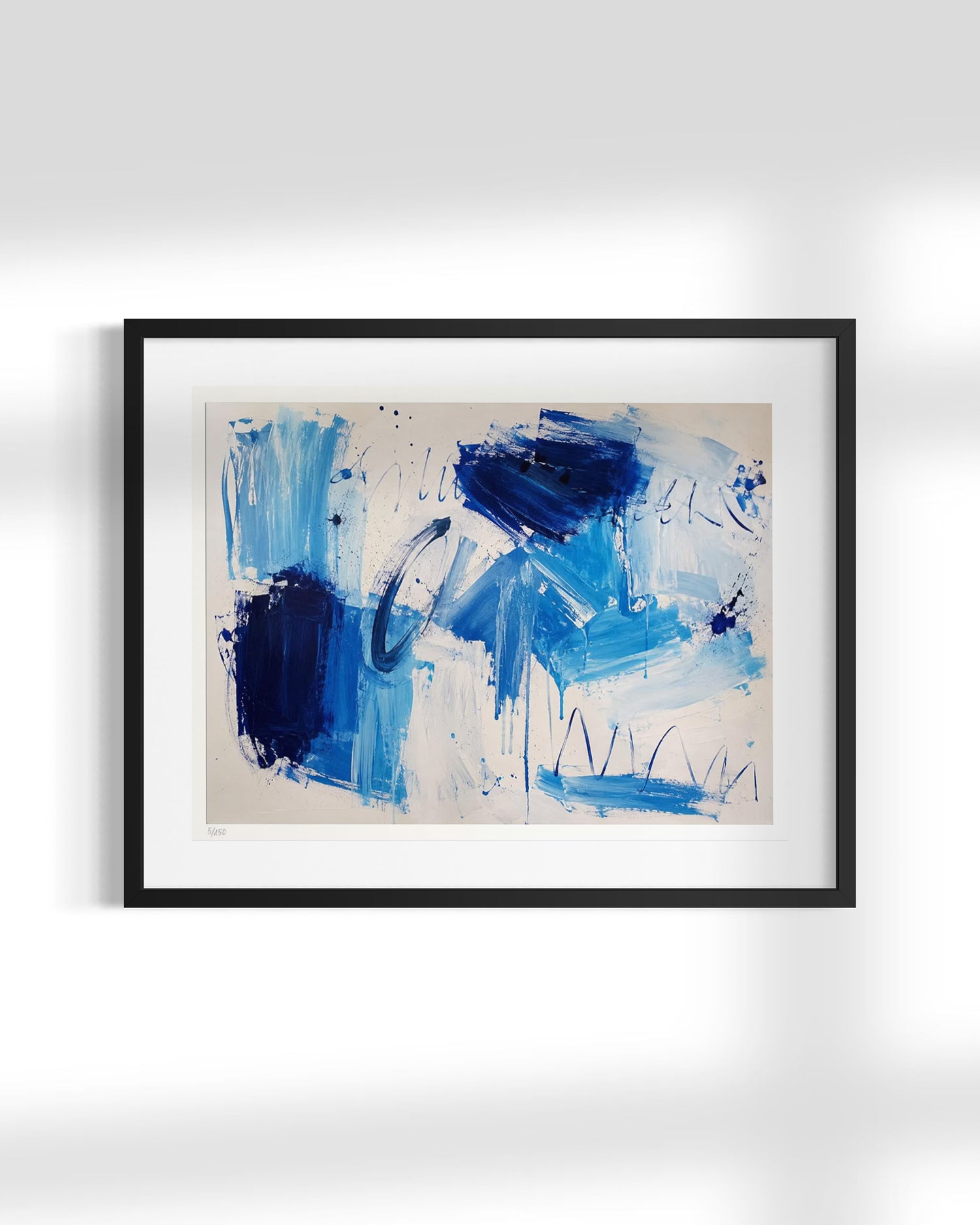 Framed abstract art print featuring expressive blue and navy brushstrokes on a cream background, enclosed in a black frame with a white mat, displayed against a light gray wall.