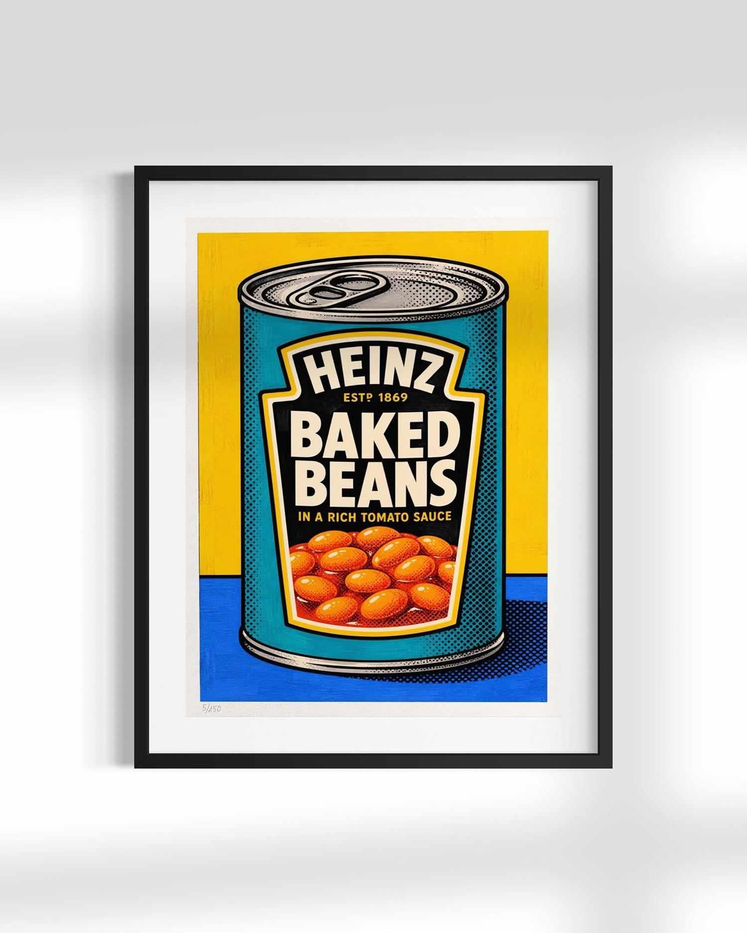A framed pop-art print of a Heinz Baked Beans can, featuring a bold yellow and blue background with the beans illustrated in the center, shown hanging on a light gray wall.